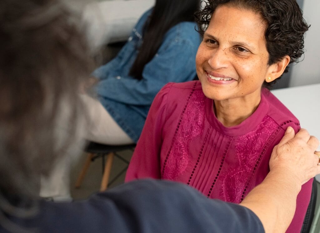 A health worker places her hand on the shoulder of a smiling woman