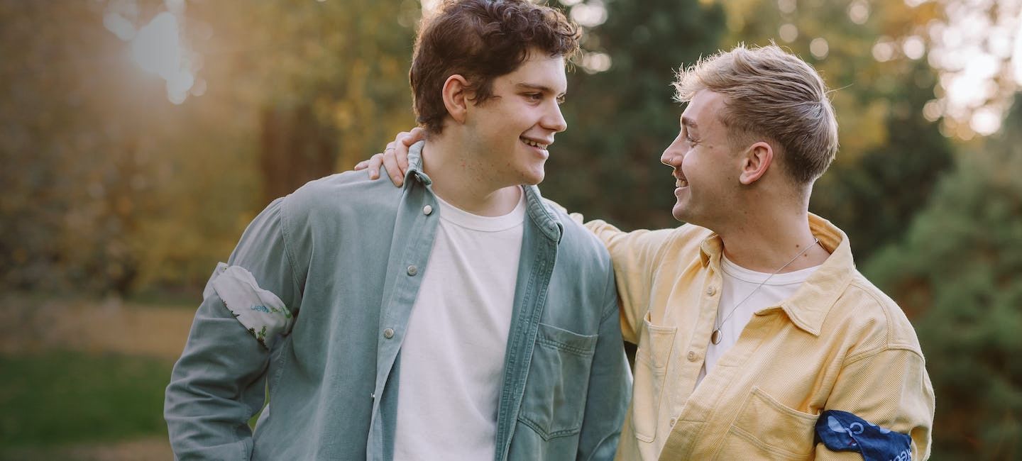 Screen shot from Canteen website showing two young men standing outdoors in a park, smiling at each other with arms around each other’s shoulders