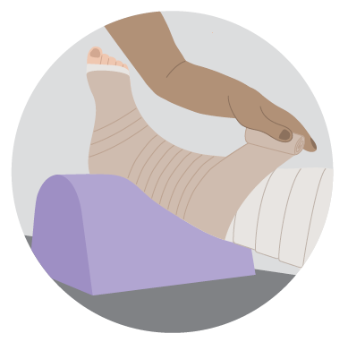 Compression bandage wrapped around a lower leg and foot, with a hand adjusting the bandage while the leg rests on a support cushion.